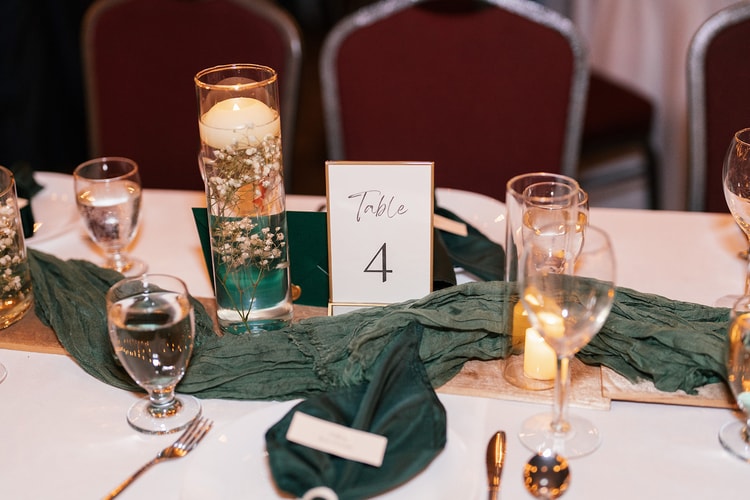 Reception table detail: a floating-candle centerpiece, green table runner, gold flatware, and a "Table 4" card under warm light.