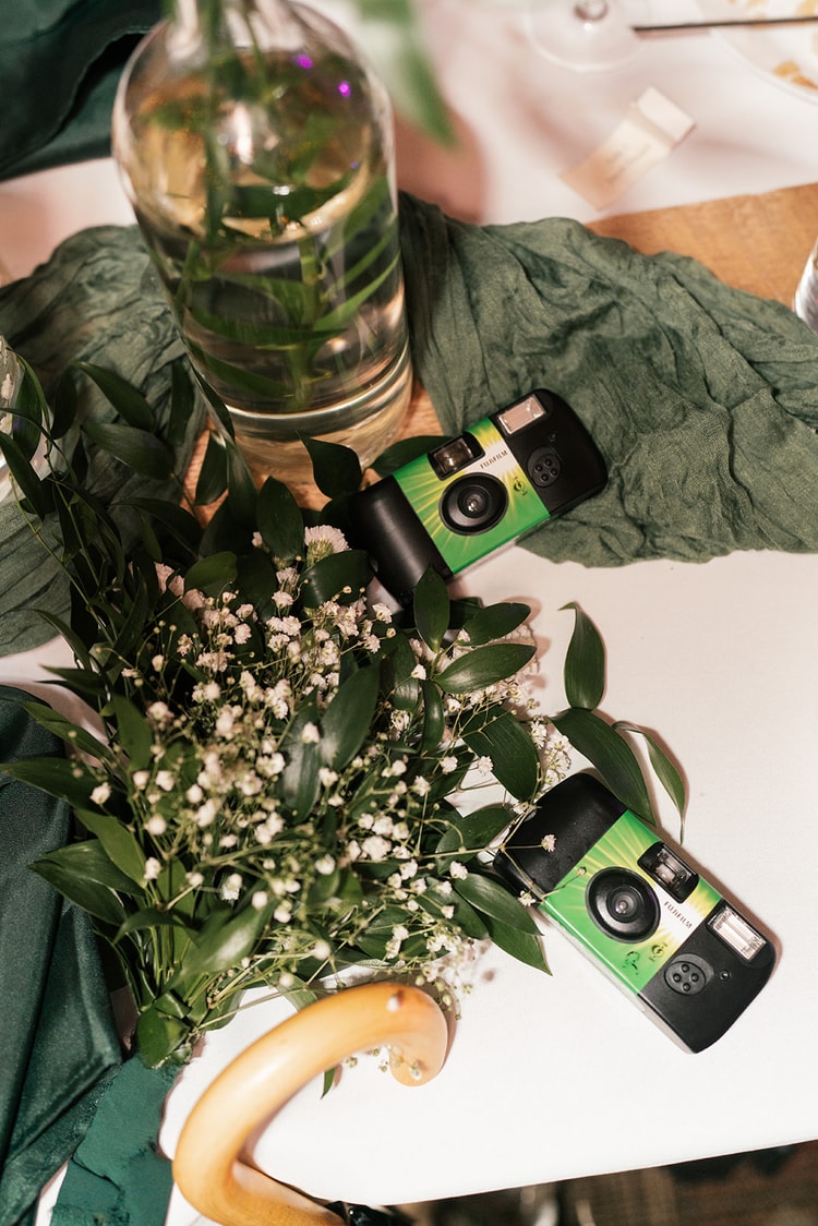 Two disposable Fujifilm cameras rest beside a baby's breath centerpiece and a green linen table runner at the reception.