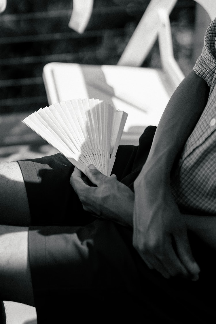 Black-and-white detail of a guest holding an open paper fan during the outdoor ceremony on a sunny day.