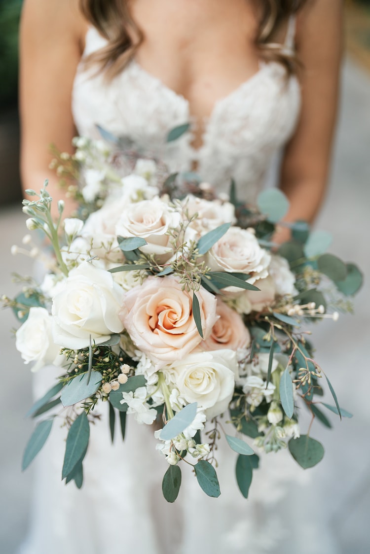 Close-up of the bride holding her loose, cascading bridal bouquet of blush and ivory roses with eucalyptus greenery.