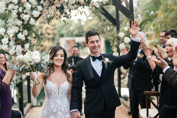 Newlyweds walk back down the aisle hand in hand, laughing and waving to cheering guests after the ceremony.