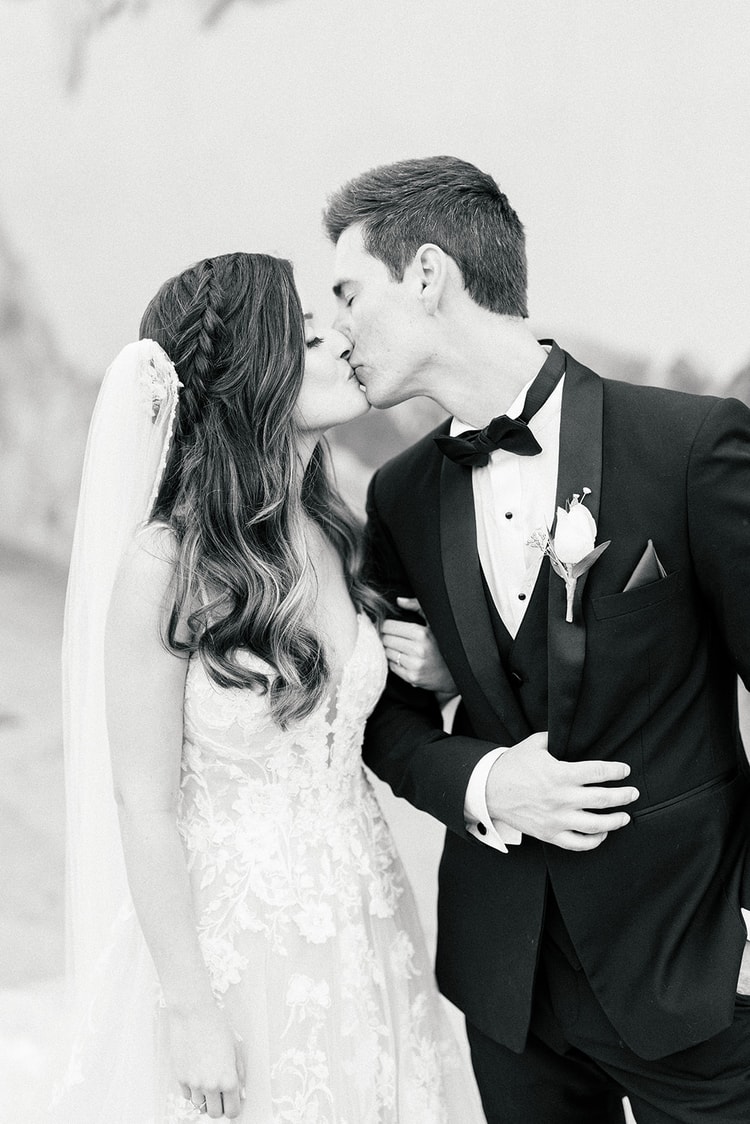 Couple standing hand in hand on a wooden deck overlooking the reception setup, gazing into the distance together.