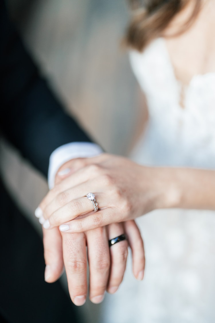 Detail of the couple's hands resting together, both wedding bands visible, bride's diamond ring catching soft light.