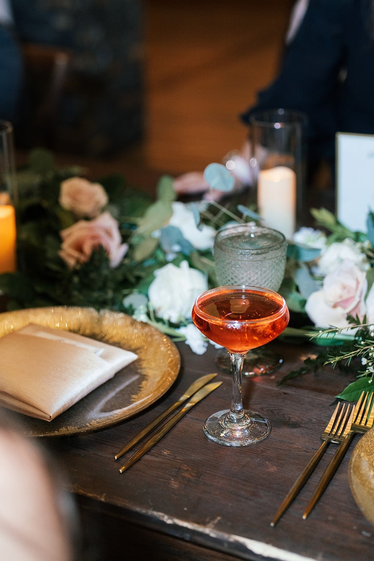 Sparkly beaded clutch resting on a reception table beside a gold charger plate and green goblet, florals in the background.