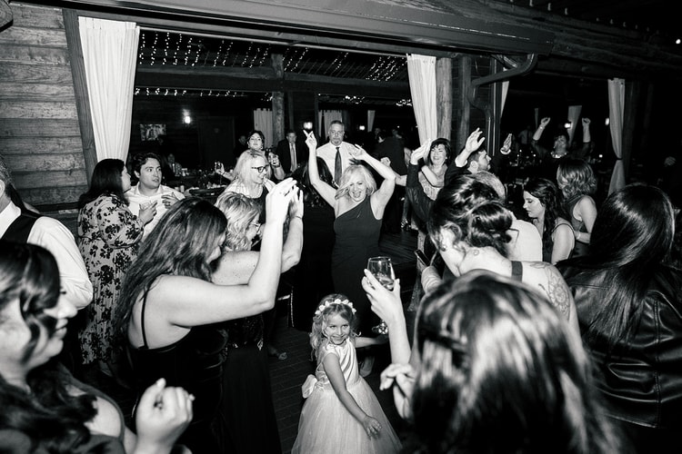 Black and white reception dance floor scene packed with guests celebrating, a flower girl standing wide-eyed at the center.