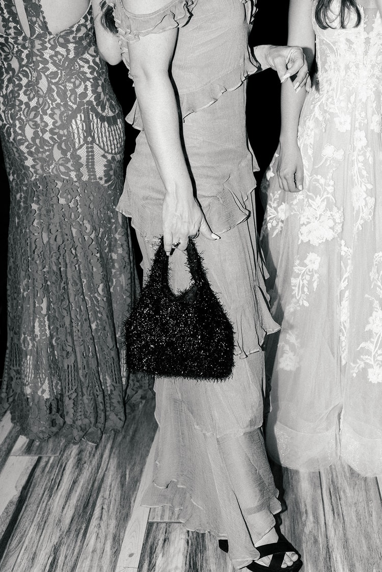 Black and white reception candid of three guests in formal dresses, one holding a small beaded bag on the dance floor.