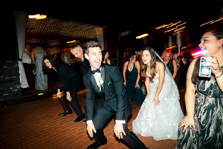 Bride and groom walk through a sparkler send-off tunnel at night, guests lining both sides as the couple beams with joy.