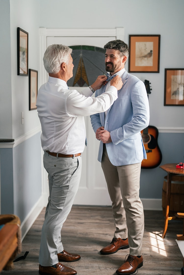 An older man helps Jacob with his bow tie as he buttons his blue jacket