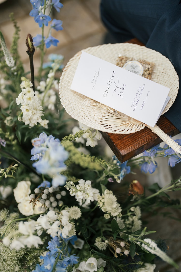 Wide view of guests seated under live oak trees at an outdoor ceremony with blue and white floral aisle decor