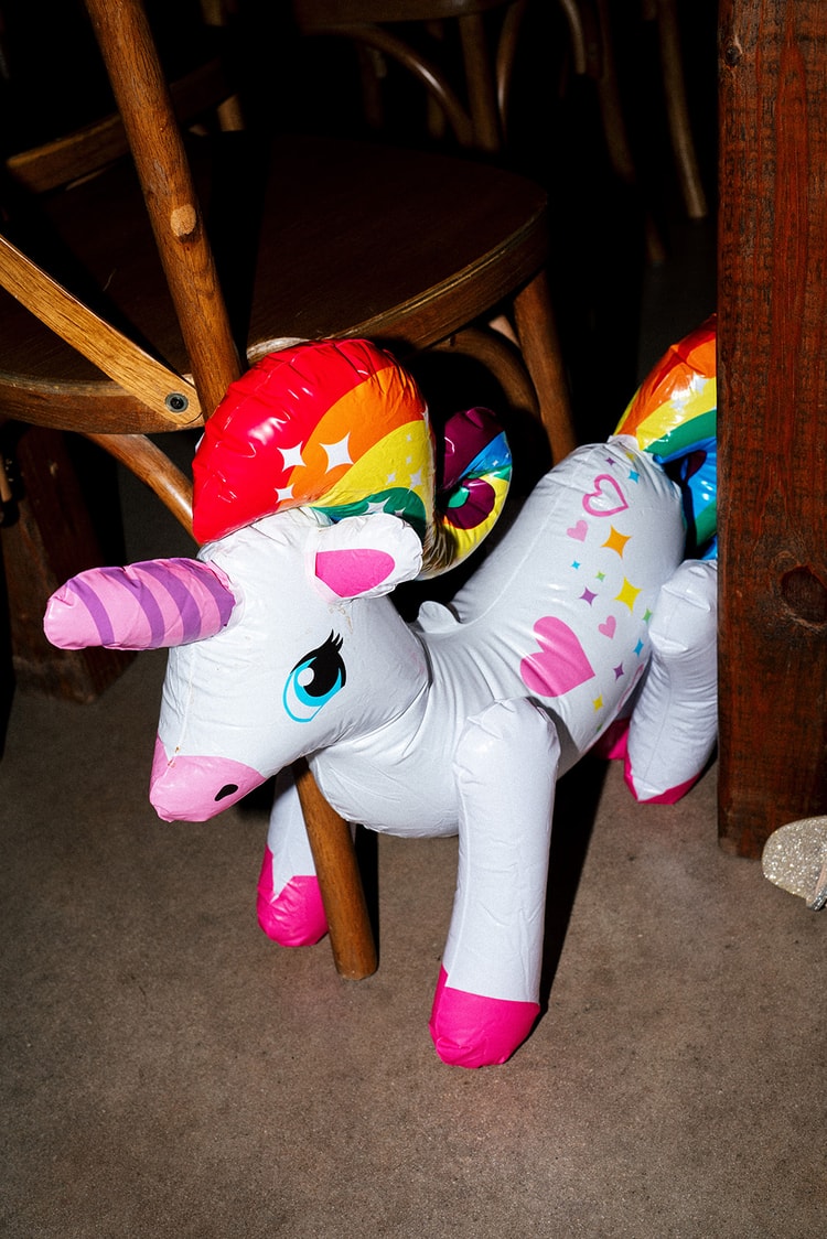 Inflatable rainbow unicorn party prop propped against wooden cross-back chairs on the reception floor, wedding details