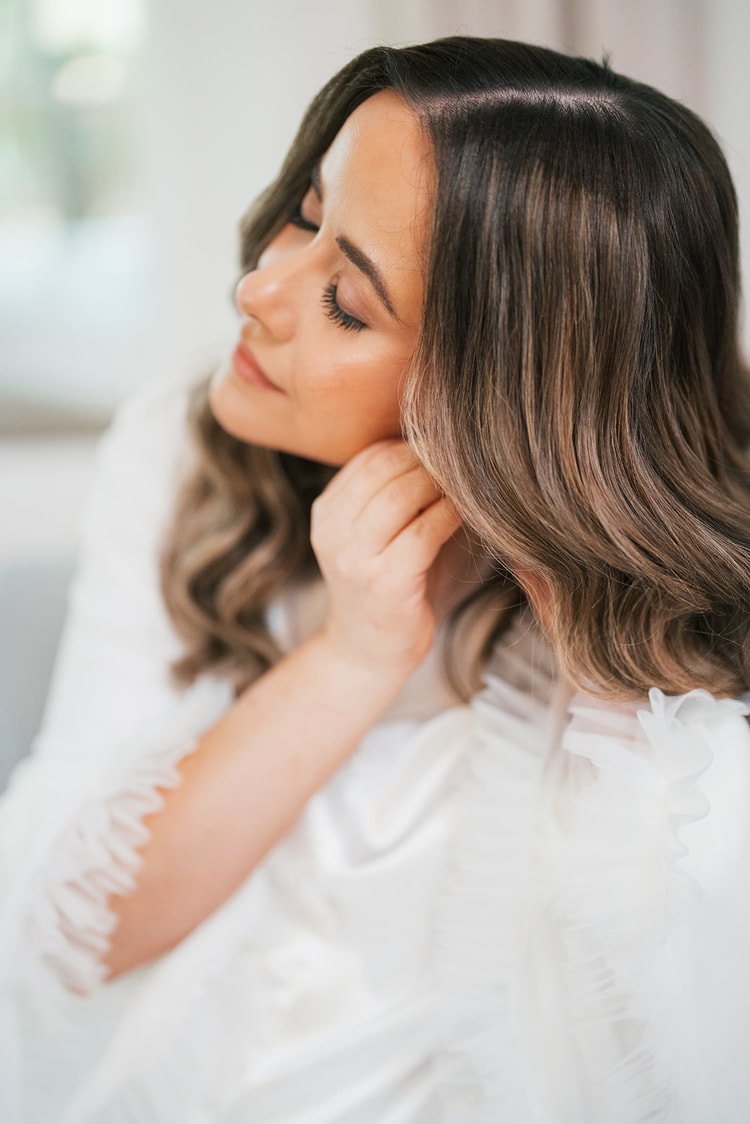 Chellsea in a white robe tucking her hair back during getting-ready in soft window light
