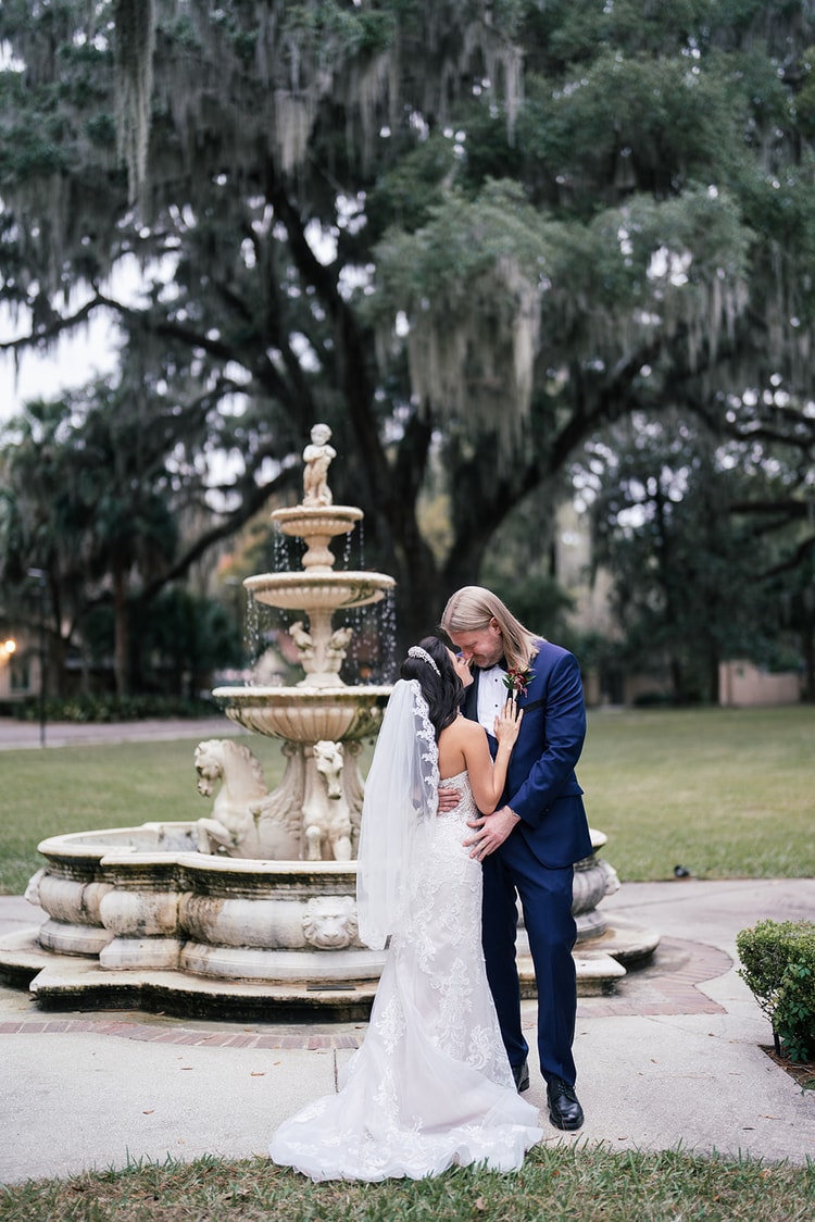 Groom holds bride close in an emotional embrace beside a tiered stone fountain