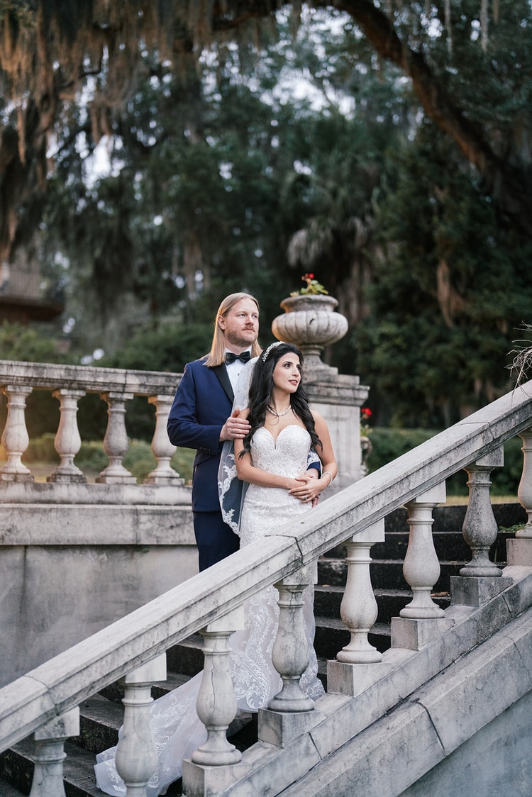 Bride and groom pause on a grand stone staircase under live oaks draped with Spanish moss, wedding photography