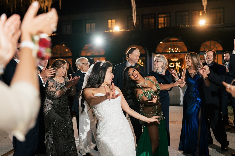 Bride and groom share a candid hug and smile with a guest at the reception venue at night