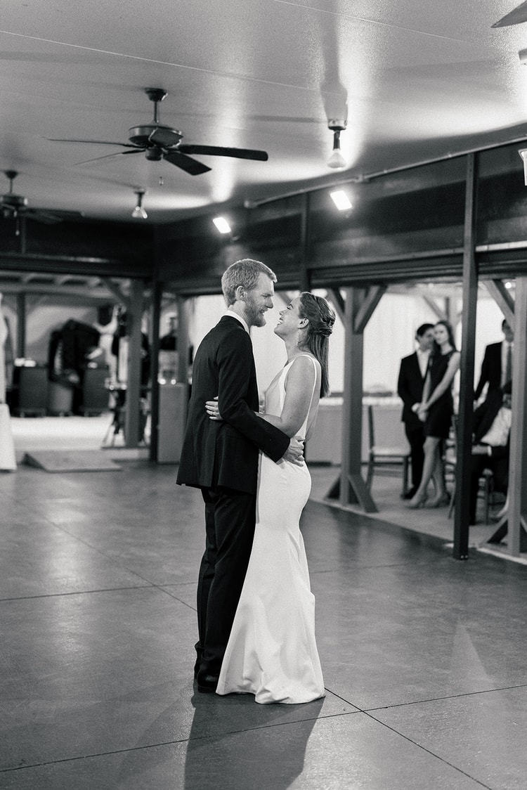 Black-and-white first dance: couple holding each other closely in the center of the dance floor, guests watching from the edges.