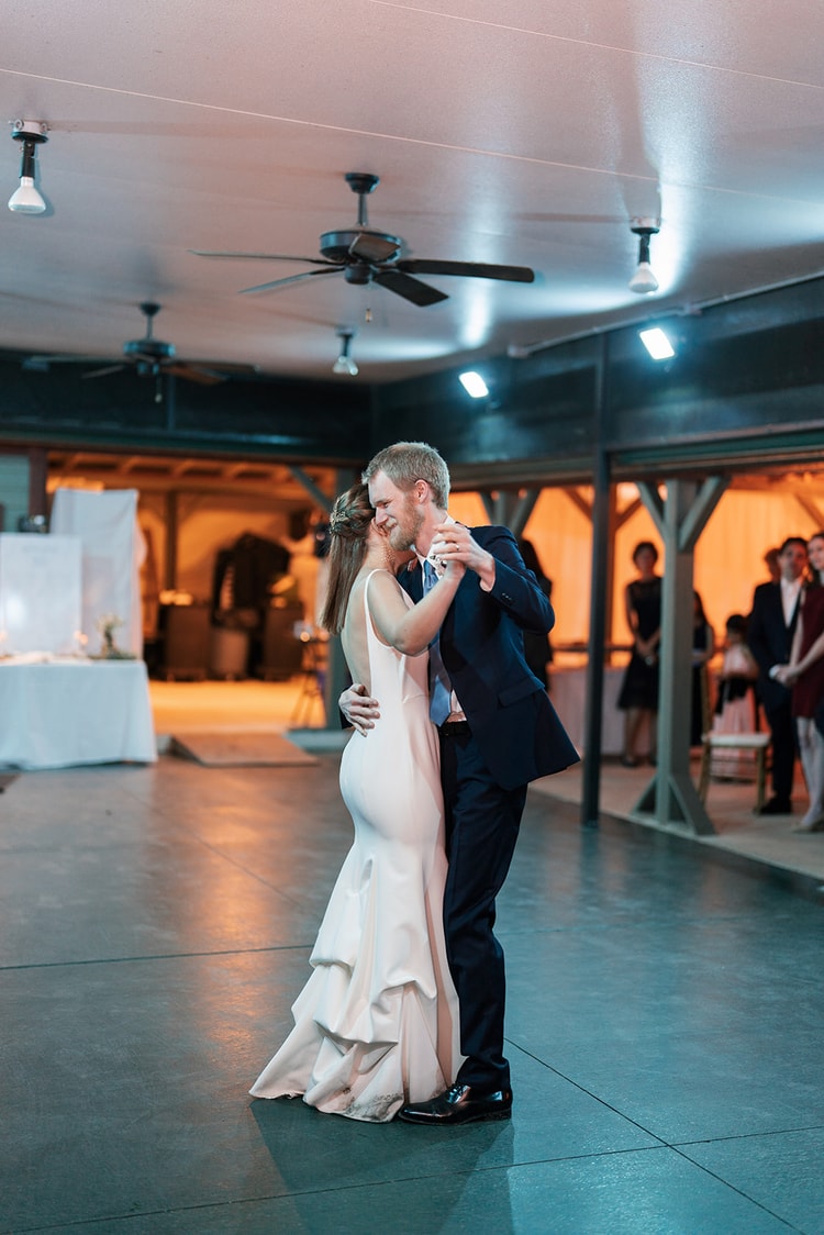 Couple sharing a close embrace and a kiss during their first dance on an open dance floor inside the reception pavilion.