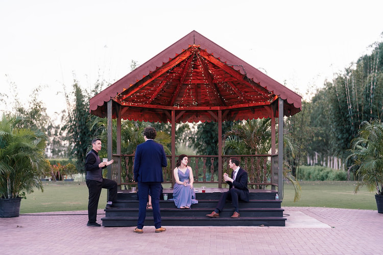 Guests mingling at cocktail hour around a lit outdoor gazebo at dusk, drinks in hand on a terracotta-paved patio.
