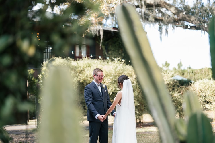 Groom laughing with delight as he sees the bride for the first time during their first look, framed by greenery and cactus.