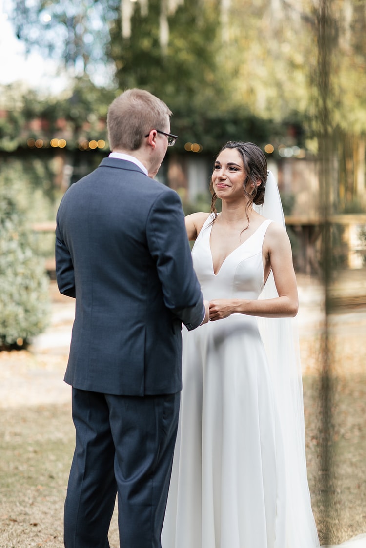 Bride and groom strolling hand in hand along a wooden walkway through tropical gardens, sharing a glance at each other.