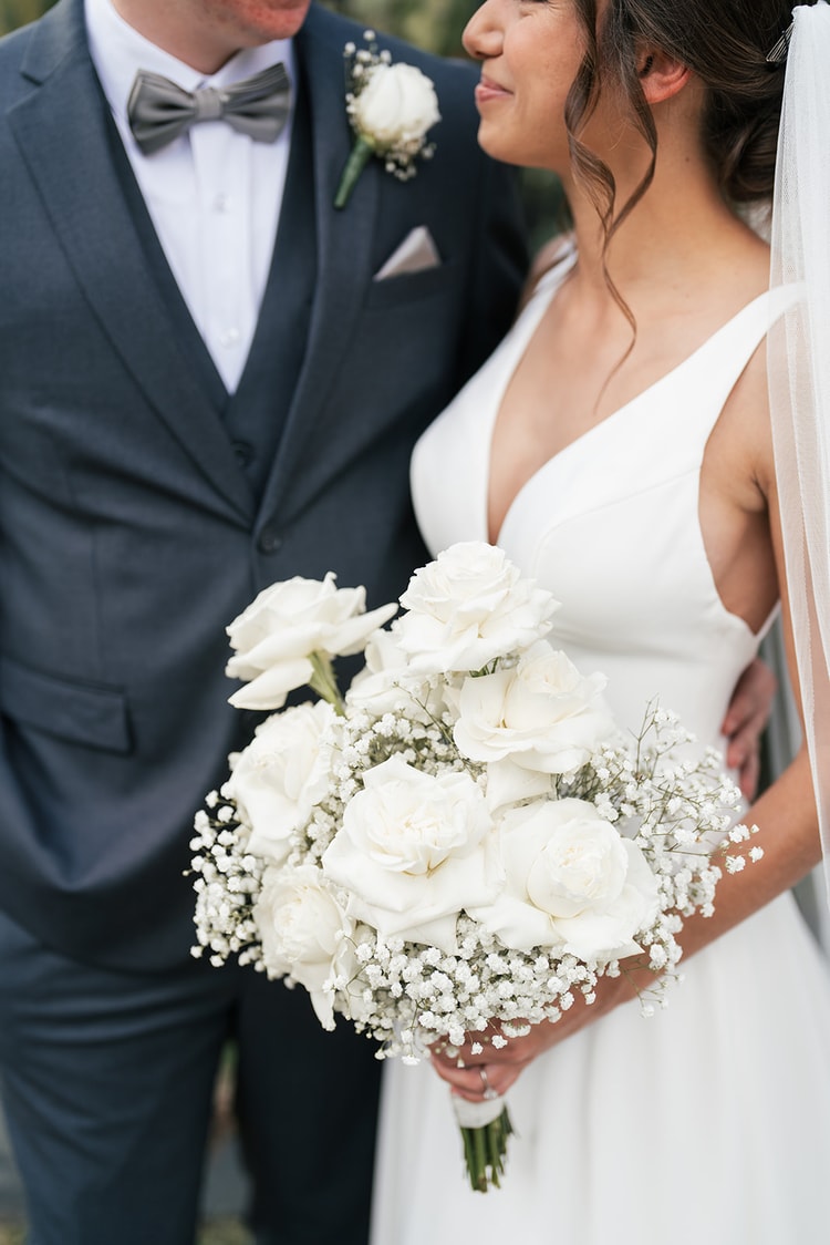 Bride and groom standing back to back, holding hands, framed by an ivy-covered arch in a garden setting.