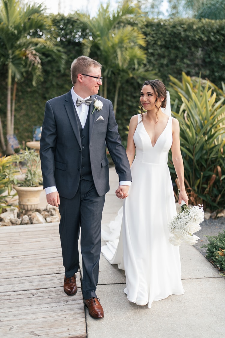 Close-up of the bride's white rose and baby's breath bouquet held against the couple's wedding attire, groom's boutonniere visible above.