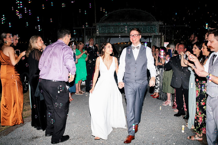 Bride and groom walking through a colorful bubble send-off, guests lining both sides cheering as they make their exit at night.