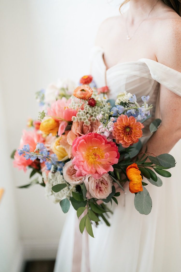 Close-up of a bridal bouquet with coral peonies, orange dahlias, blush garden roses, and ribbon streamers