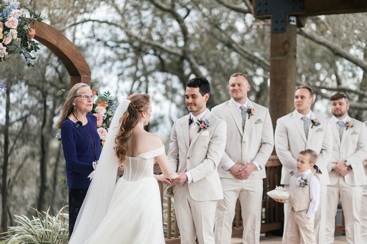 Bride and groom laugh together during their ring exchange, the handfasting cord visible between their hands