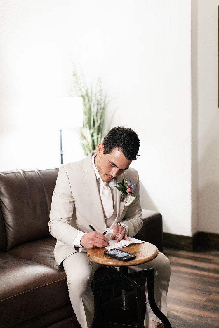 Black and white close-up of the groom adjusting his cufflink and wristwatch while dressed in his cream suit.