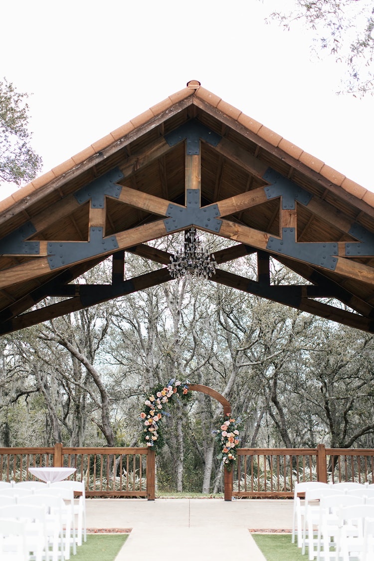 Timber-framed ceremony pavilion with a floral arch and chandelier overlooks rows of white folding chairs at Sterling Event Venue in Orlando, Florida.