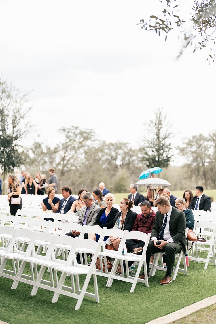 Wedding guests seated in white folding chairs on a lawn watch the outdoor ceremony at Sterling Event Venue in Orlando.