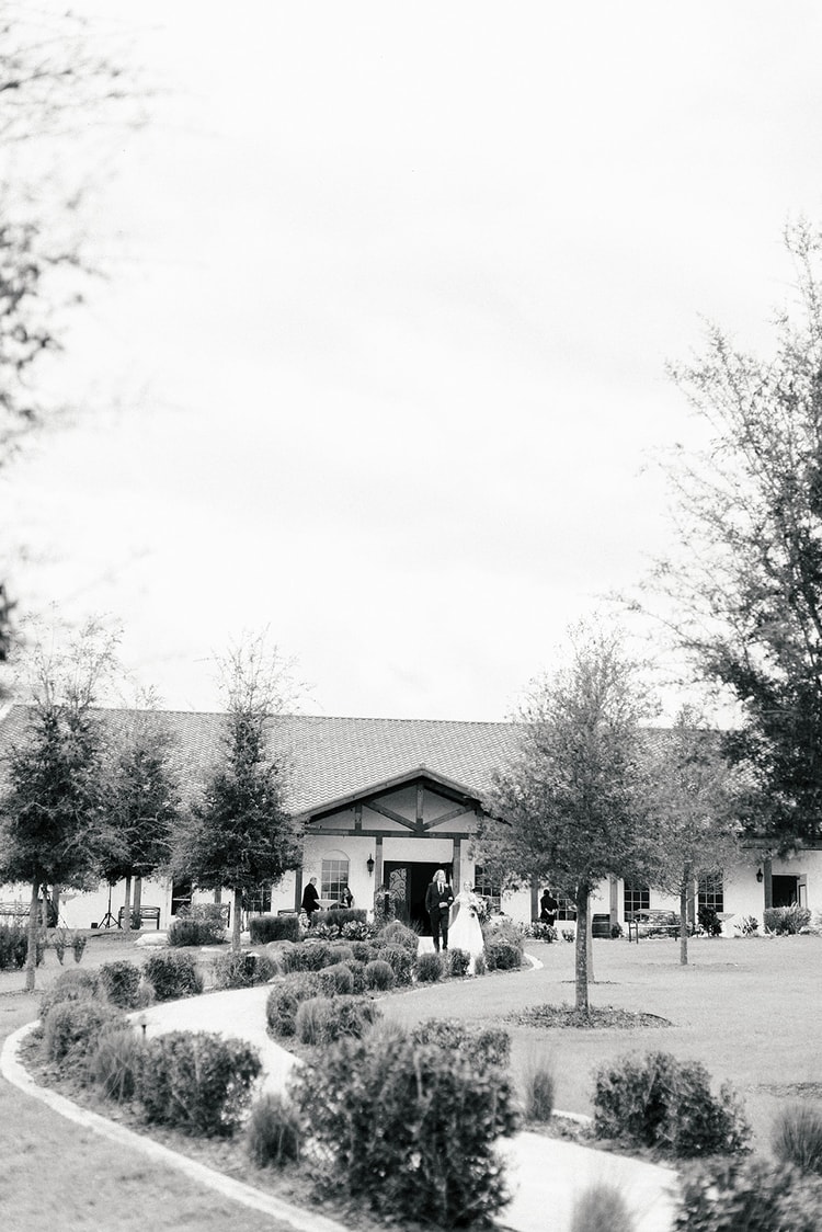 Black and white wide shot of the bride and groom walking toward the Spanish-style clubhouse before the Orlando wedding ceremony.