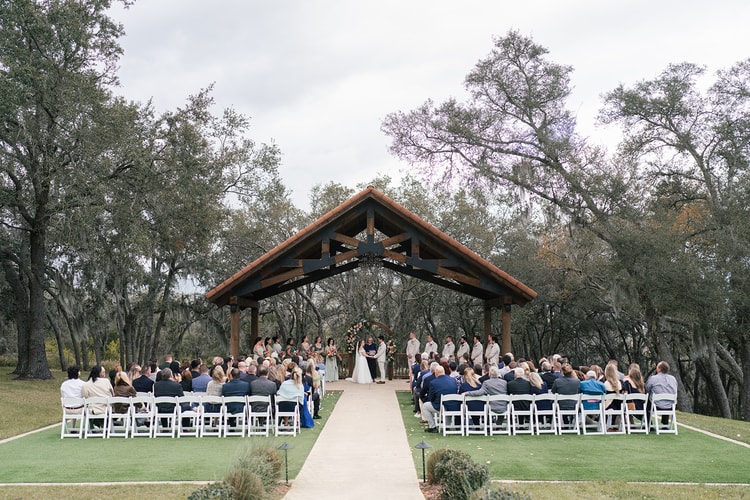 Wide aerial view of the full wedding party and guests gathered under the wooden pavilion for the ceremony at Sterling Event Venue.