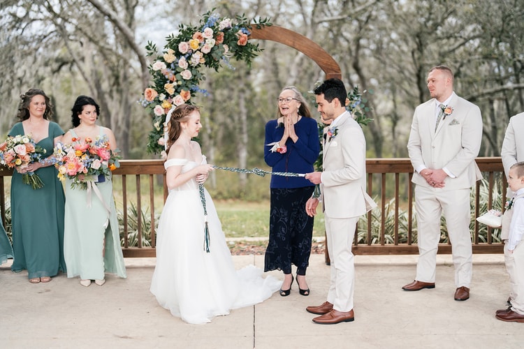Officiant claps with joy as the bride and groom hold a green and white handfasting cord during the ceremony.