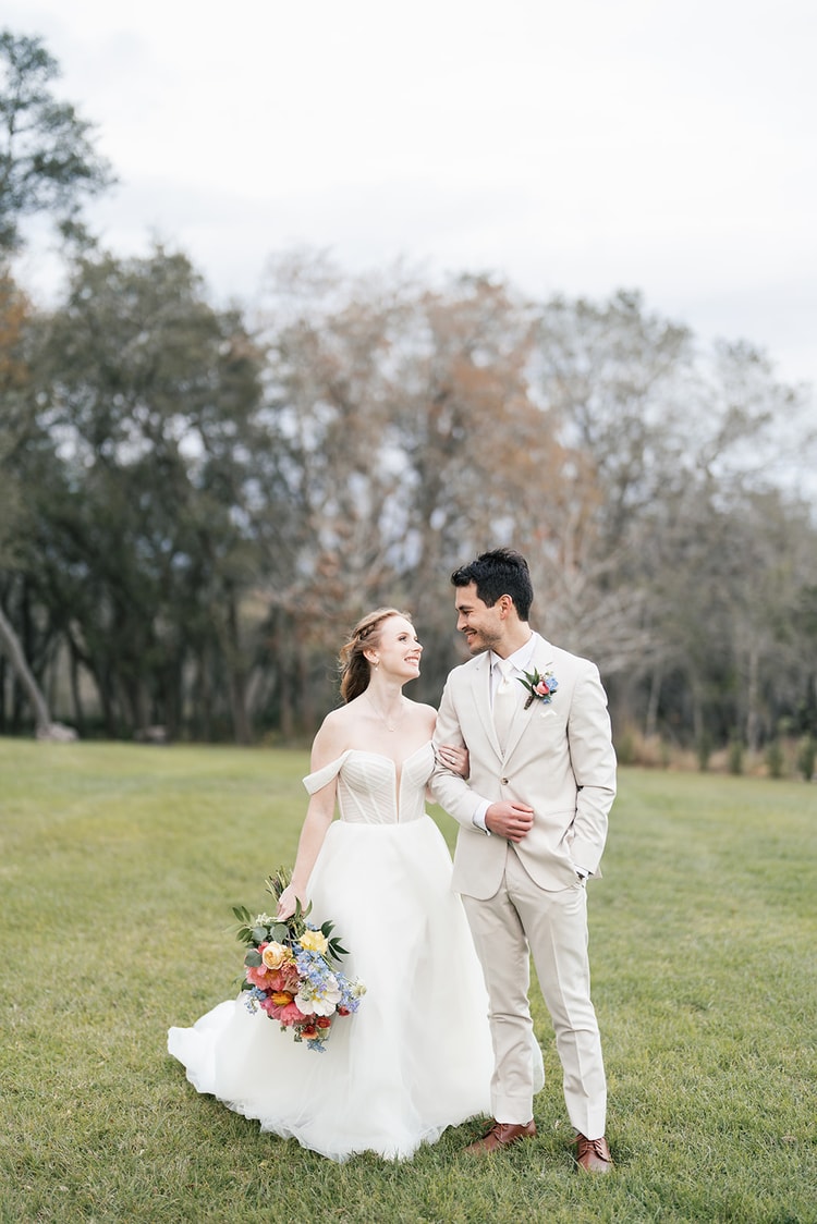 Bride and groom stand close together on the open lawn, smiling at each other in the fading evening light.