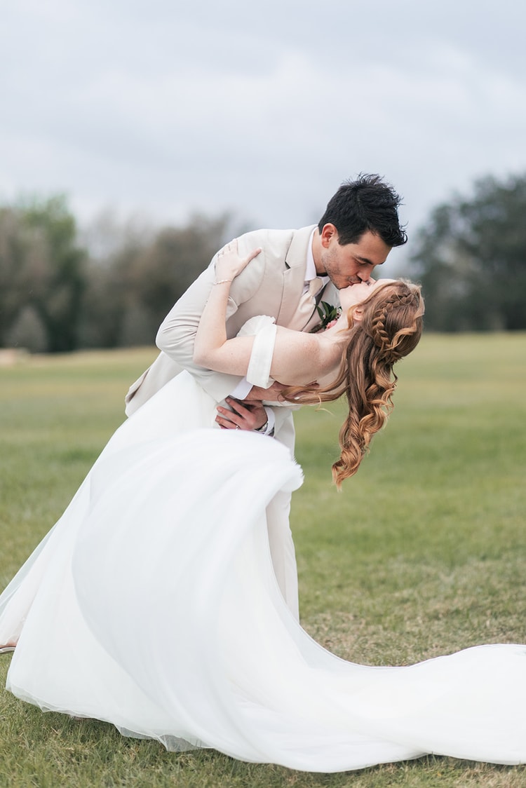 Groom dips the bride into a kiss on the open lawn at Sterling Event Venue, her tulle skirt sweeping across the grass.