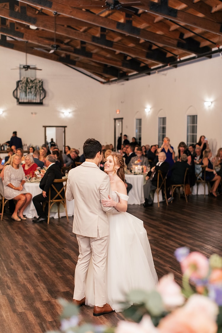 Bride and groom share their first dance on the wooden reception floor as seated guests at Sterling Event Venue watch and applaud.
