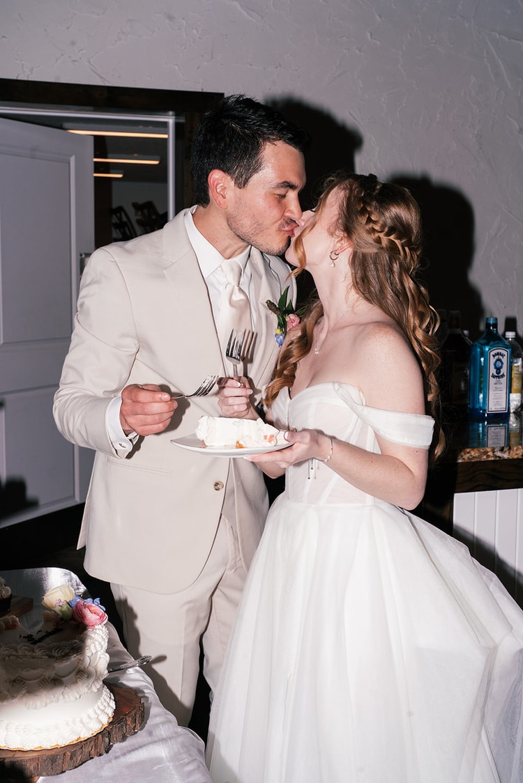 Bride and groom share a bite of wedding cake and a kiss at the reception, warm indoor light at Sterling Event Venue in Orlando.