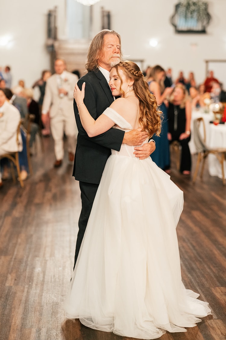 Bride rests her head against her father's shoulder mid-dance, eyes closed, at the Orlando venue reception.