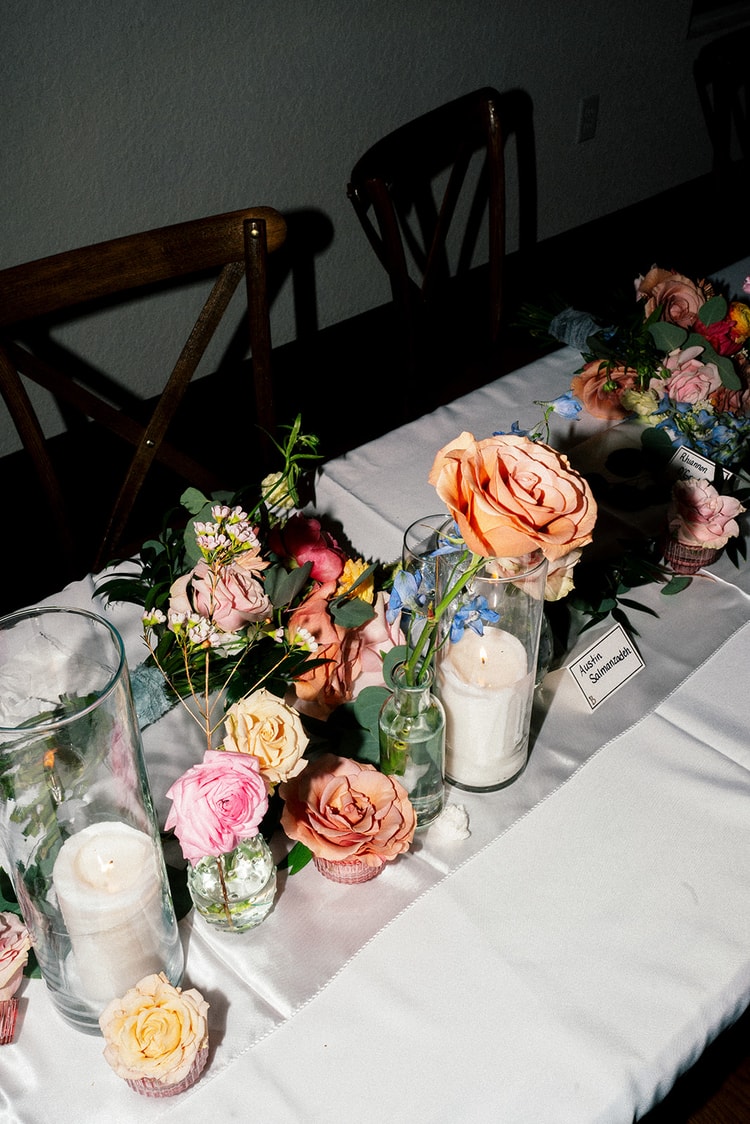 Reception table detail with roses, eucalyptus, lit candles, and a handwritten place card for a guest.