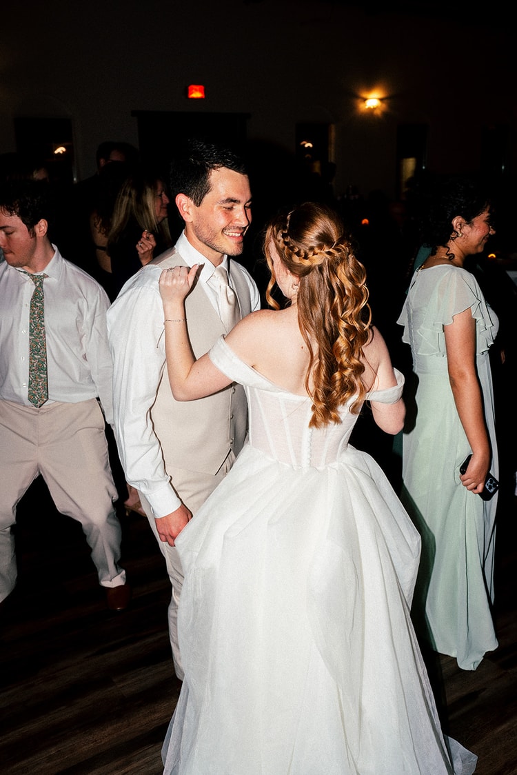 Bride and groom dance close together at the reception, her curled hair catching the low evening light.