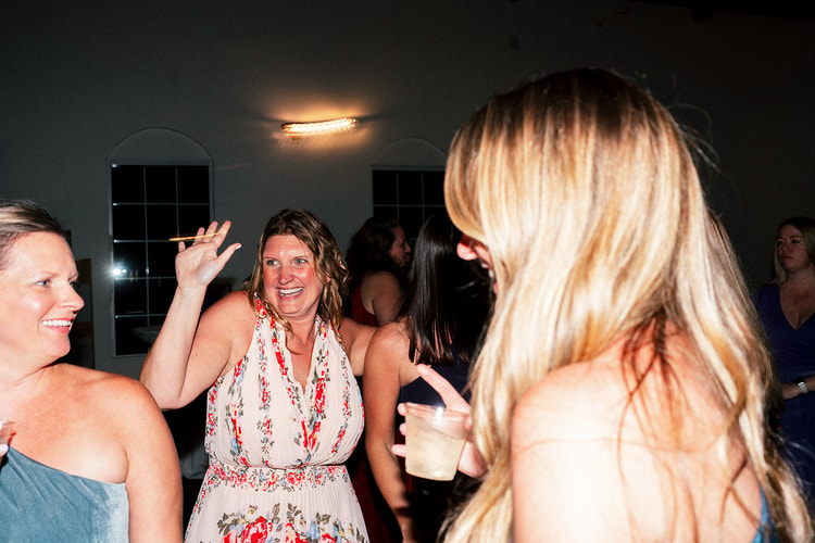Bridesmaid in a floral dress laughs and raises her hand while dancing with friends at the reception party.