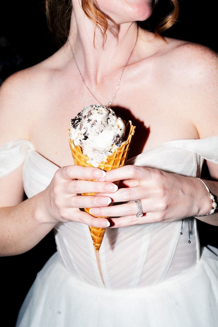 Close-up of the bride holding a waffle cone piled with cookies-and-cream ice cream against her wedding gown.