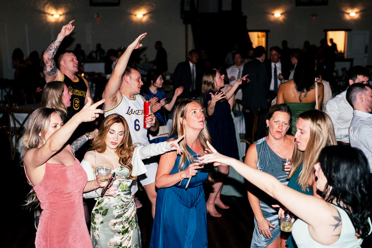 Guests dance and sing along together at the reception, arms raised, one wearing a Lakers jersey under string lights.