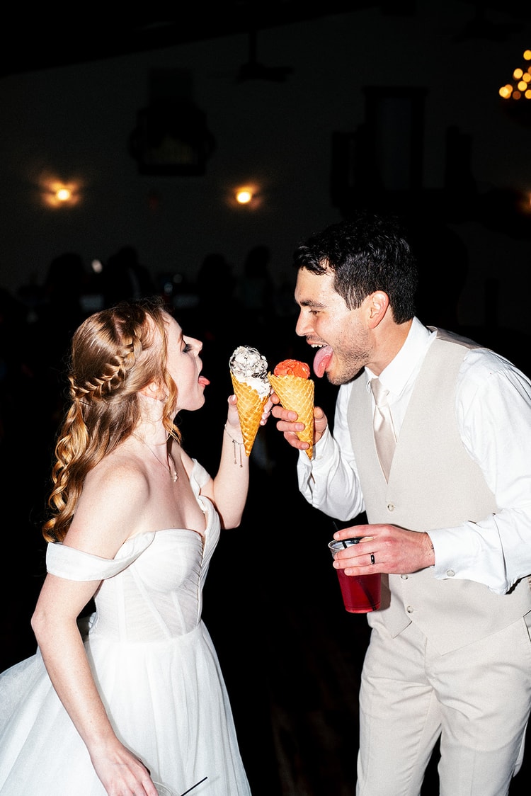 Bride and groom lean in to lick their ice cream cones together, laughing, at the late-night reception.