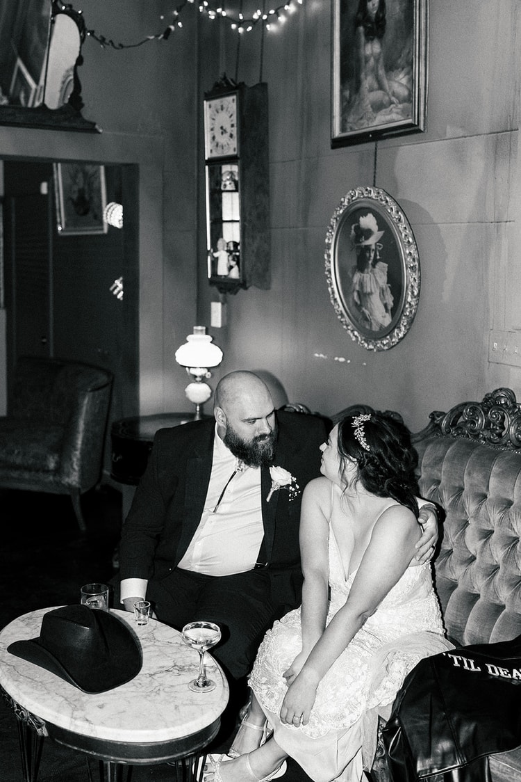 Black and white portrait of Sydney and Manny seated close together in a vintage lounge with framed art